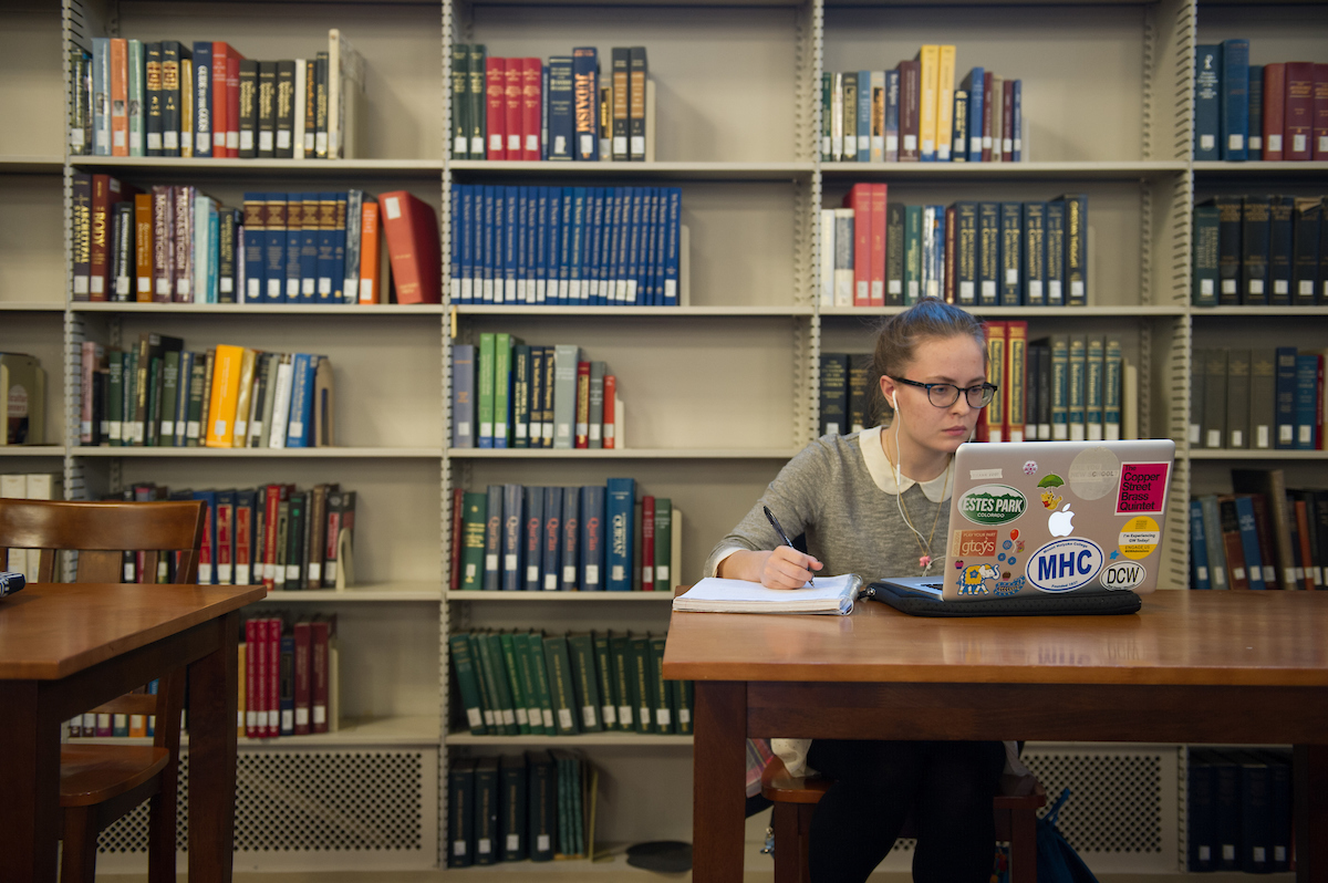A student working in the library with a notebook and a laptop