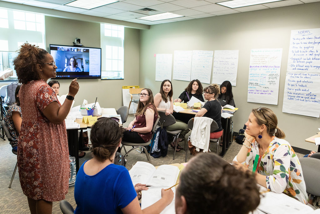 MATM students in a classroom discussion with a digital screen displaying other engaged students.