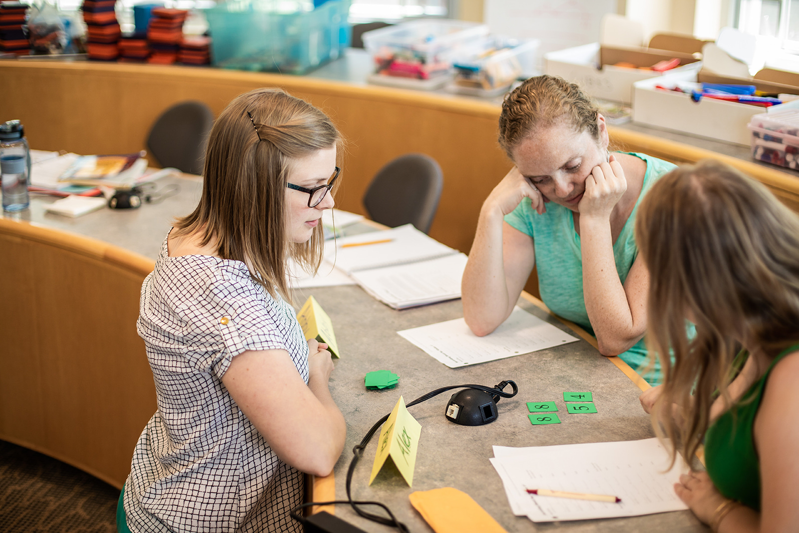A group of three PaGE students looking at numbers on green cards on a table.