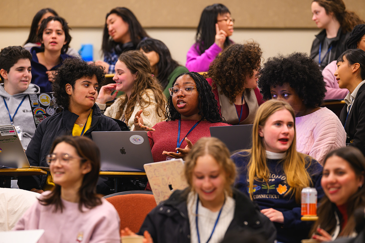Students sit in rows of a classroom, many in discussion.