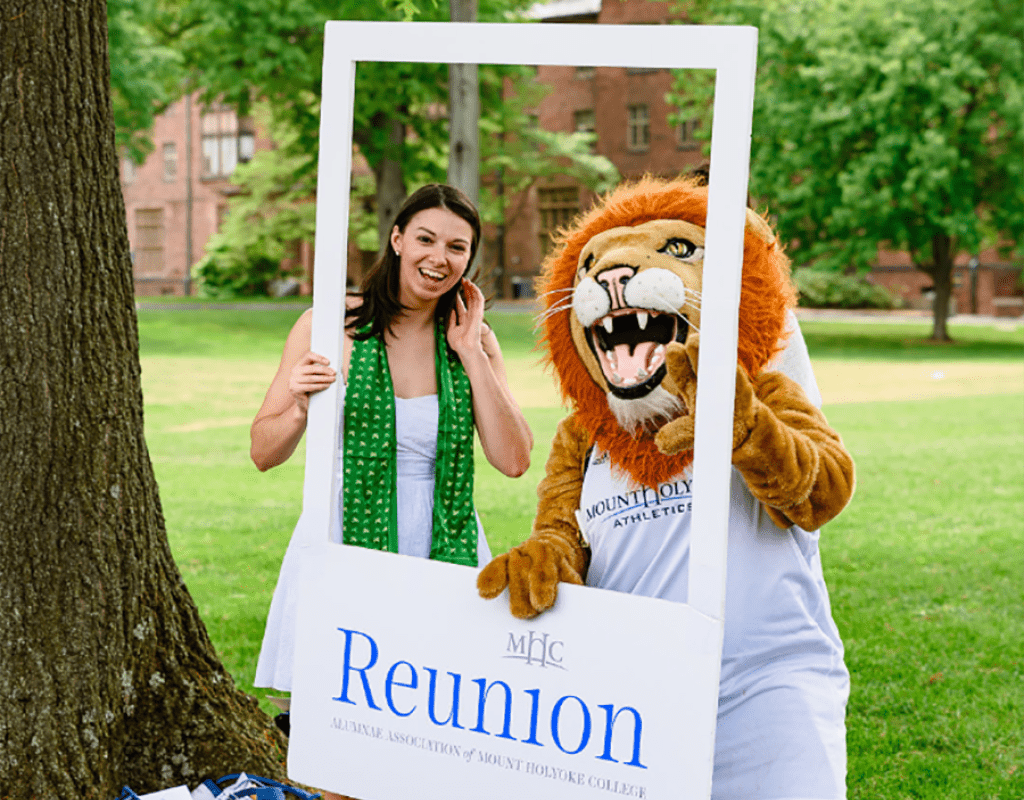 Anl alum posing in a photo frame with Paws, the Mount Holyoke College mascot