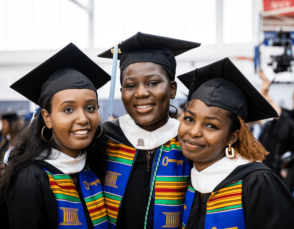 Three happy graduates in caps and gowns preparing for Commencement 2023