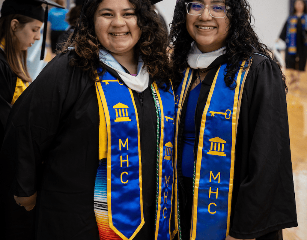 Two smiling graduates wearing caps, gowns and stoles