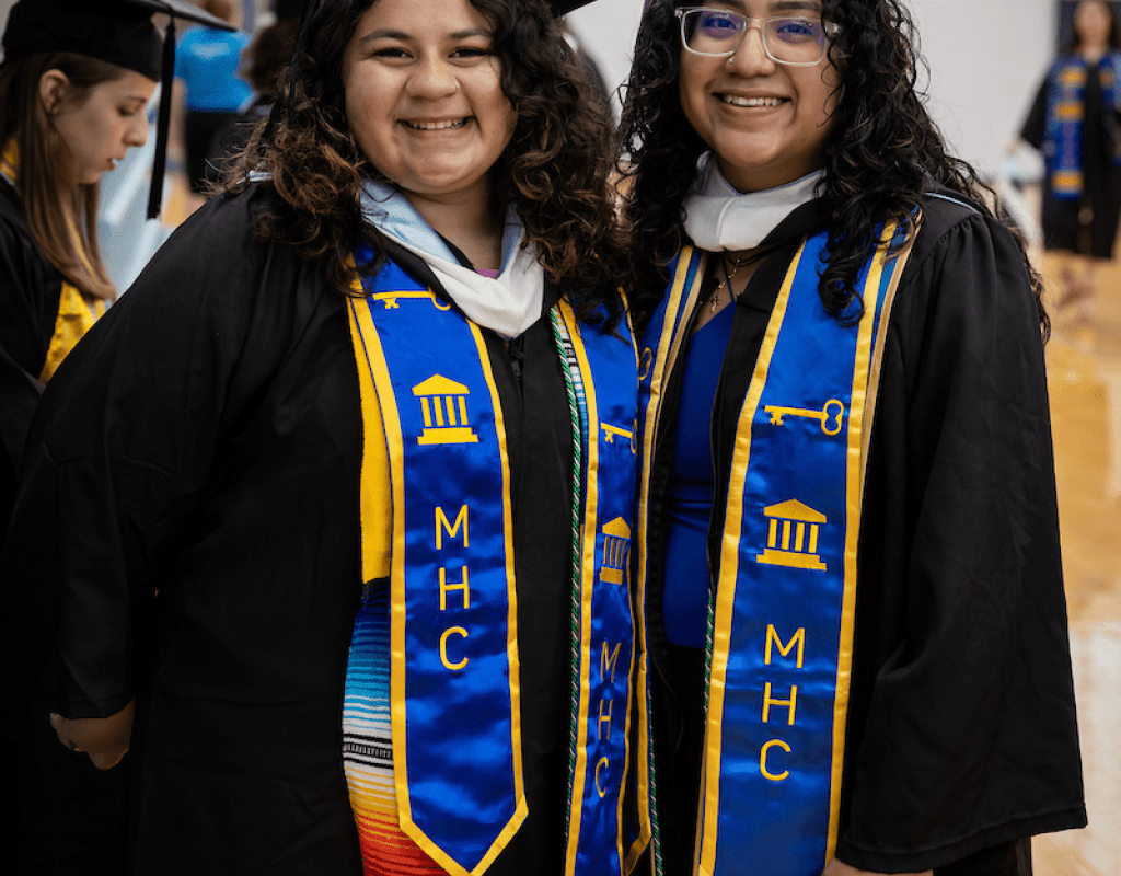 Two smiling graduates wearing caps, gowns and stoles