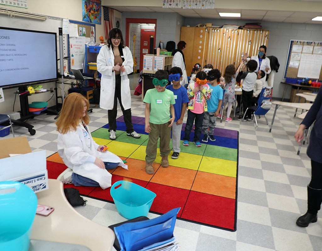 MHC students look on as first grade students try goggle brain activity.