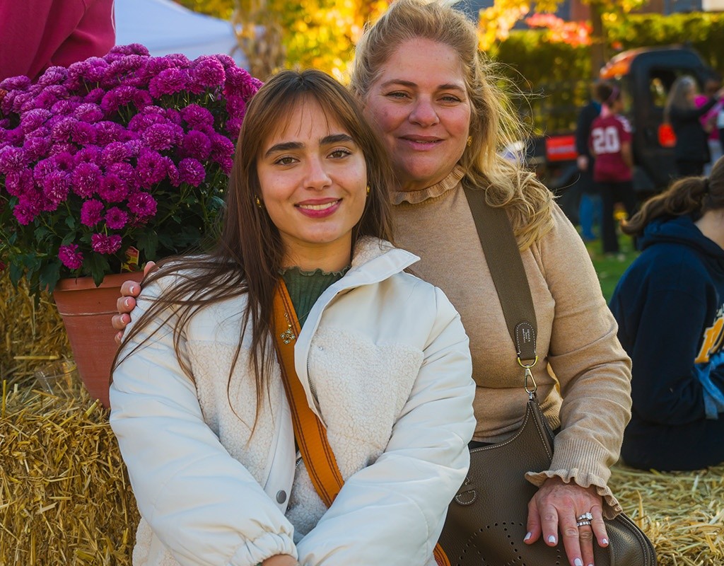 Student and family member sit on decorated hay bales at Mount Holyoke's Fall Fest in 2024.