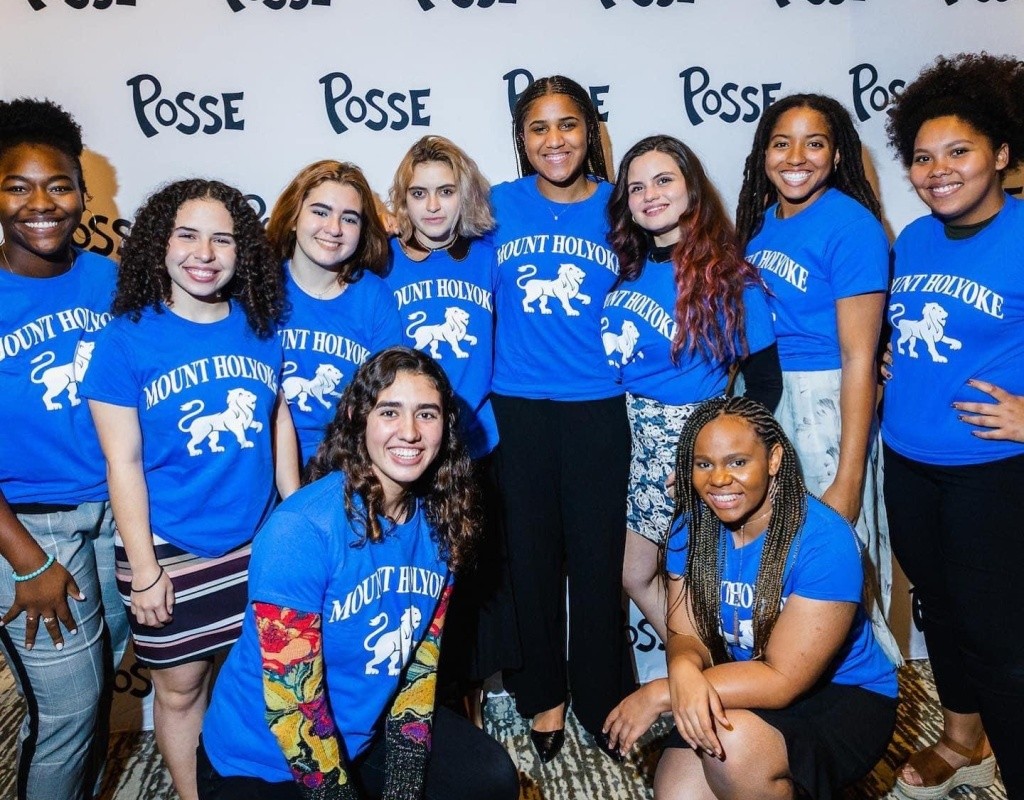 Posse scholars pose together in matching Mount Holyoke shirts, Posse Foundation logo behind them.