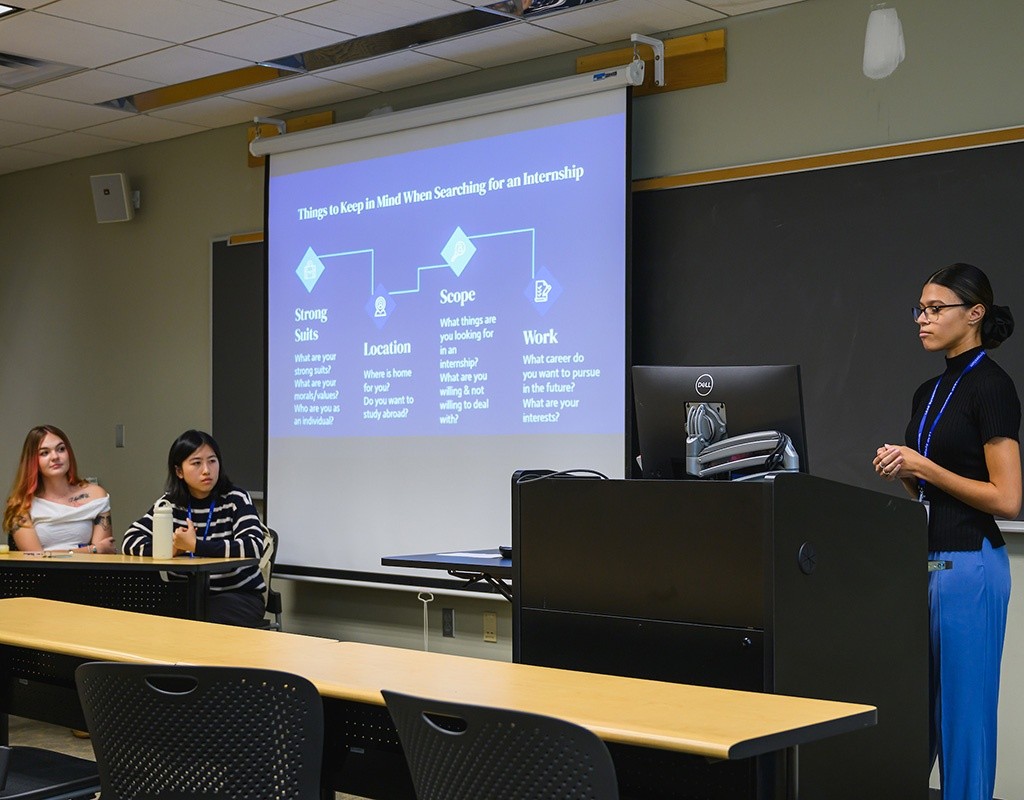 LEAP Presenter in front of a podium, with a screen presentation on the side. LEAP 2024, Mount Holyoke College
