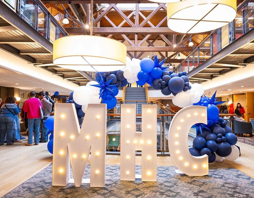 White letters MHC with lights, and blue balloons in the Community center for Experience MHC! April 5, 2025, Photo by Jo Chattman.