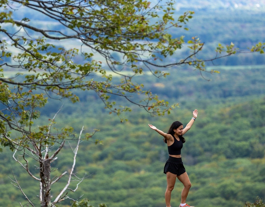 A student raises their hands atop a rock on the Mt. Holyoke summit.