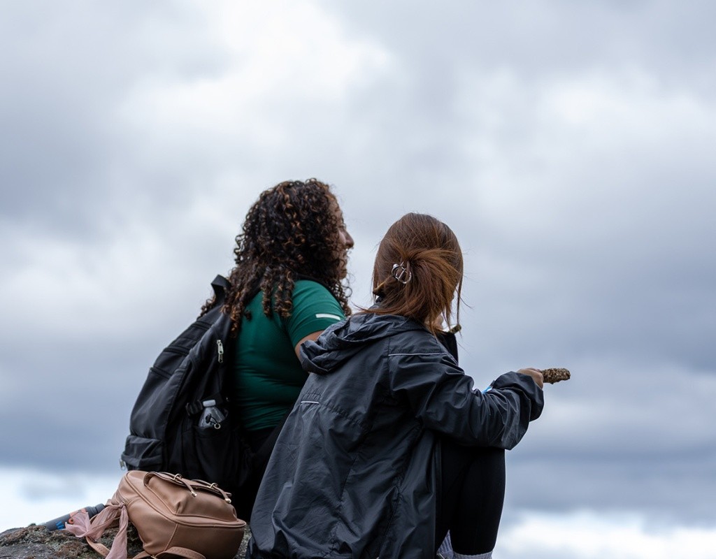Two students sit atop a rock looking out over the valley at the summit of Mt. Holyoke.