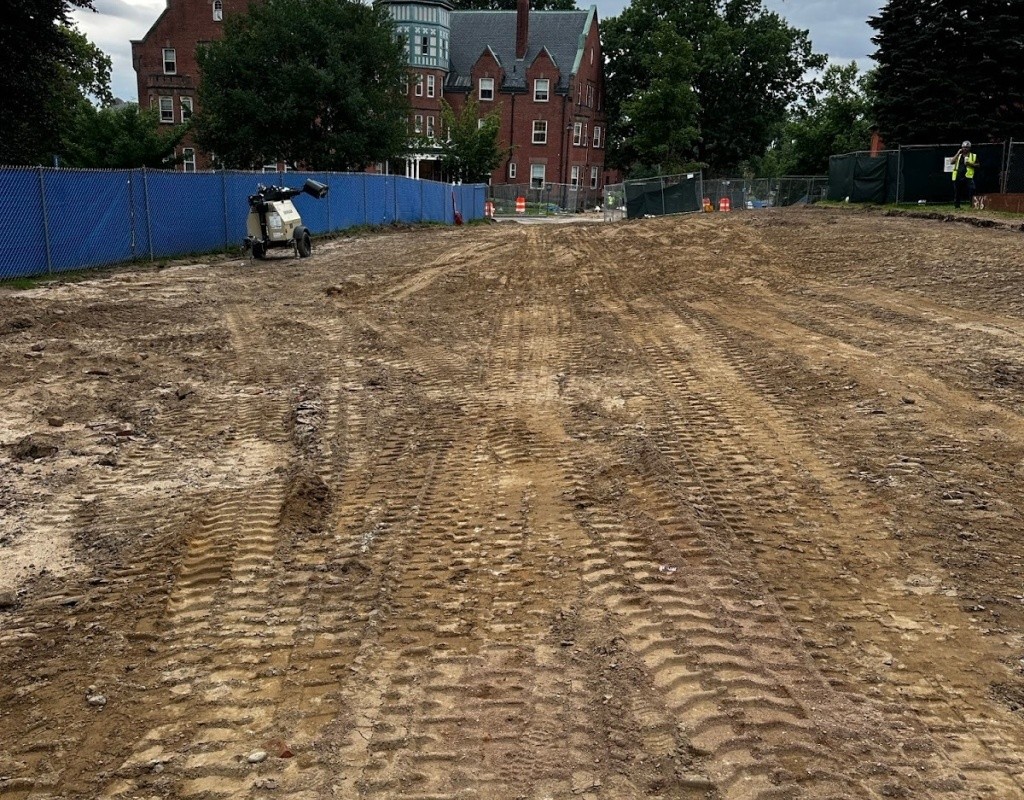 Tire tracks in the dirt with construction fencing and the residential building in the background.