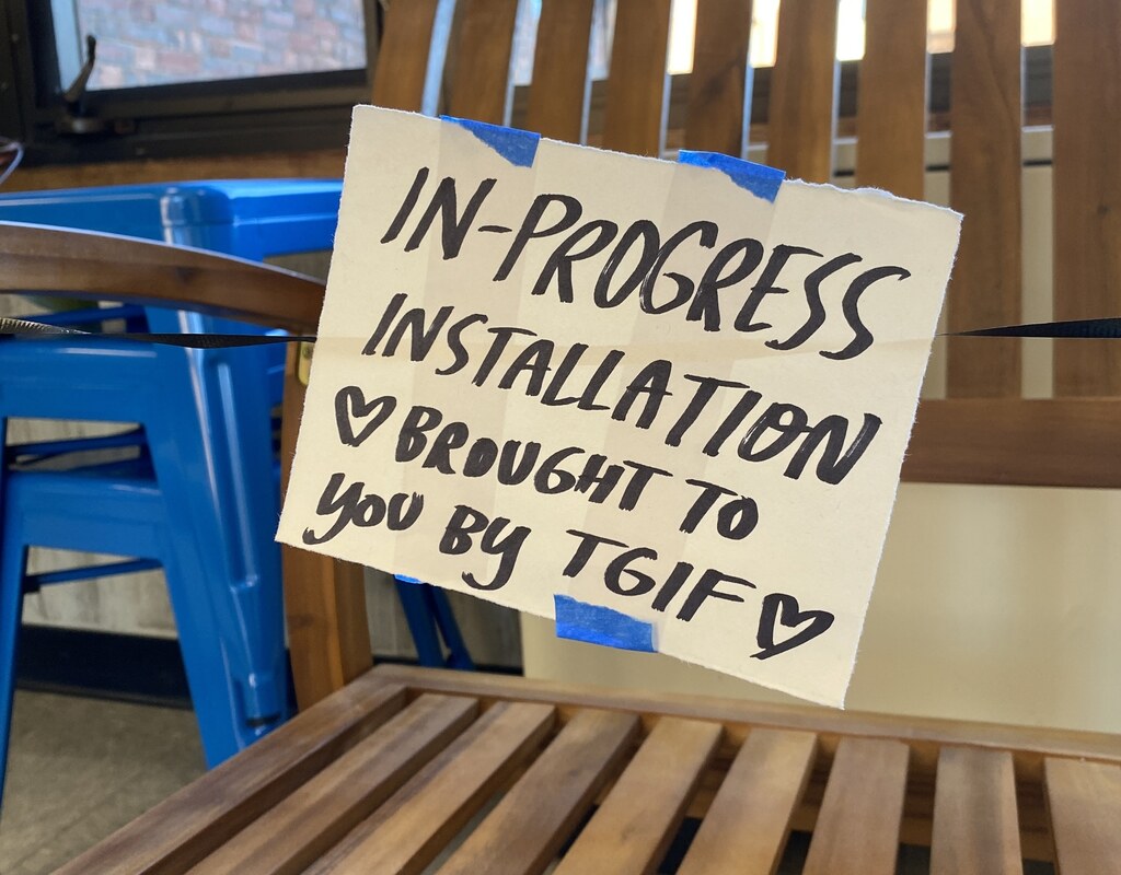 A sign on a chair in the Art Building Lobby "In Progress Installation brought to you by TGIF"