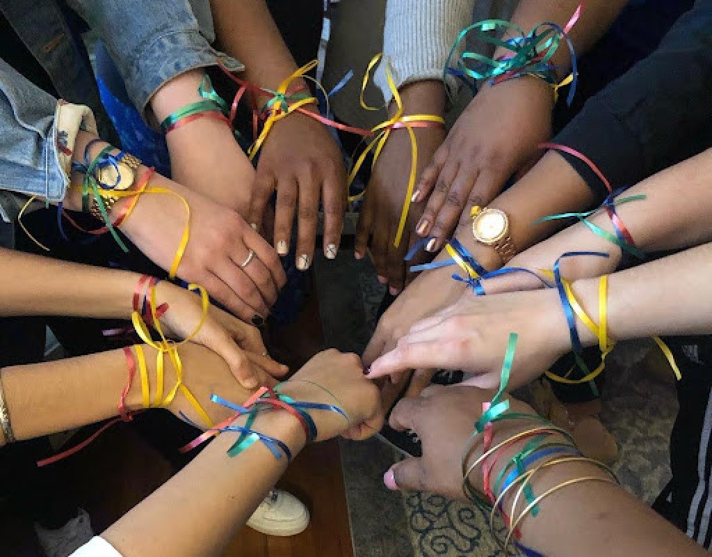 Posse scholars with ribbons on their wrists snap photo with hands together in a circle.