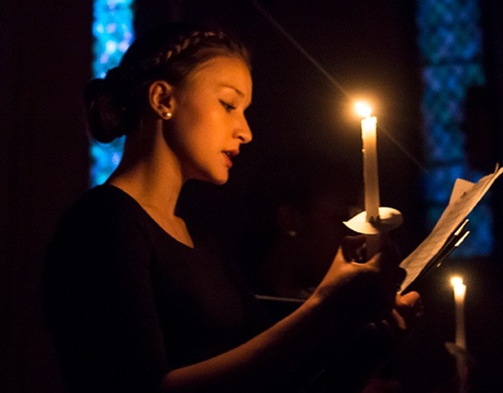 A singer uses candlelight to view music during a Vespers concert