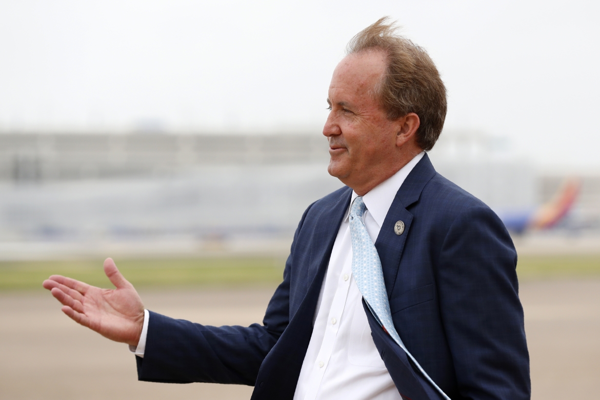 Ken Paxton, balding, waiting on a tarmac, tie flapping in the wind, gesturing 