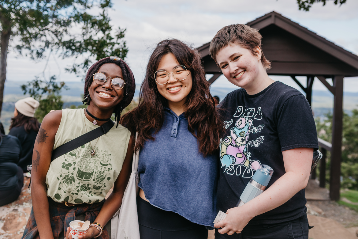 Three students smiling widely on the top of Mount Holyoke on Mountain Day 2022