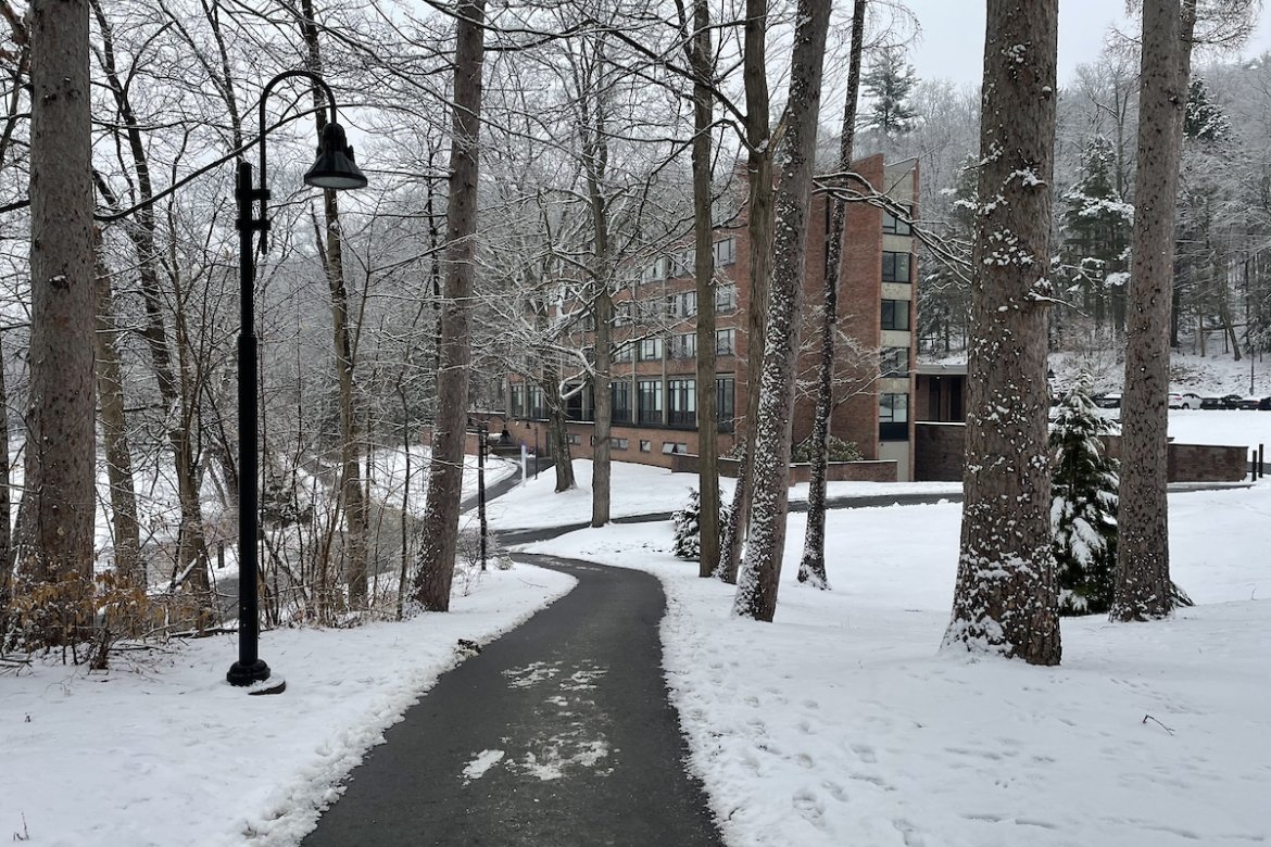 An empty, plowed path on campus on a snowy day. A residence hall can be seen in the distance.