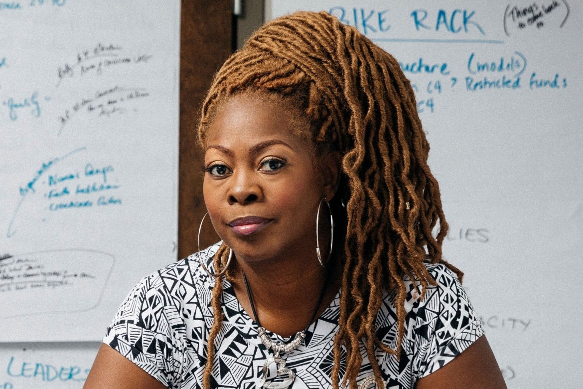 LaTosha Brown, in front of a whiteboard, with a black and white short-sleeved shirt.