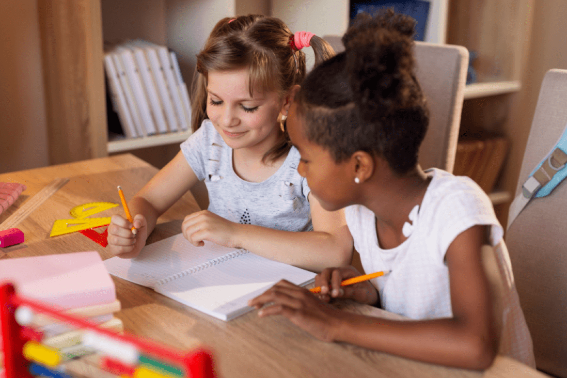 Two students looking at a blank notebook with math paraphernalia around them on the desk.