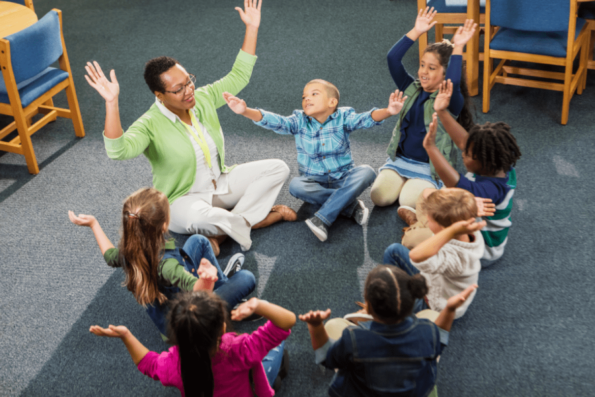 Engaged students in a circle raising arms with their teacher.