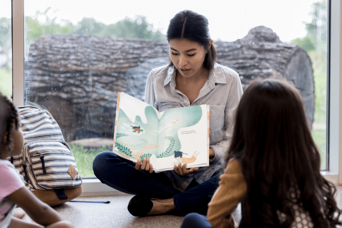 Woman reading book to students. Stock photo courtesy Canva.