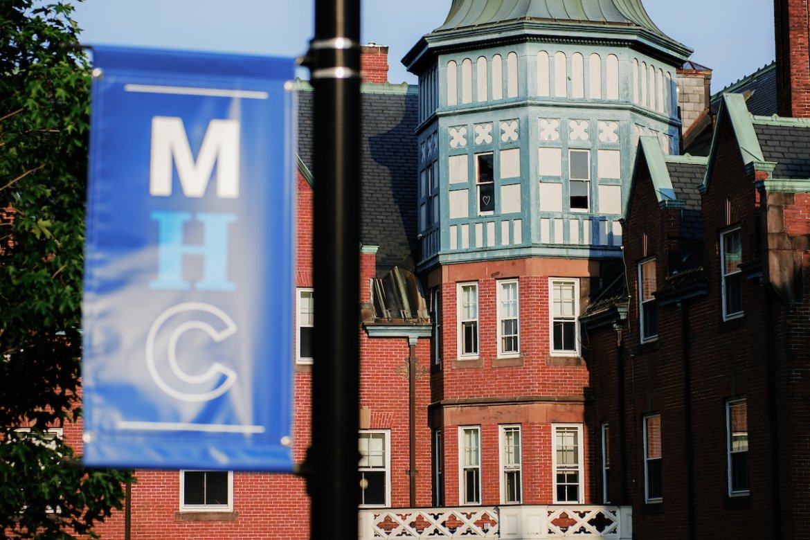 Mount Holyoke Campus during the summer of 2024 - a banner on a pole out of focus with a brick building with pretty architectural details in the background