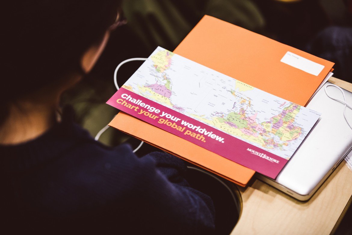 A look over a student's shoulder, laptop and flyer in view, it reads: Challenge your worldview. Chart your global path.