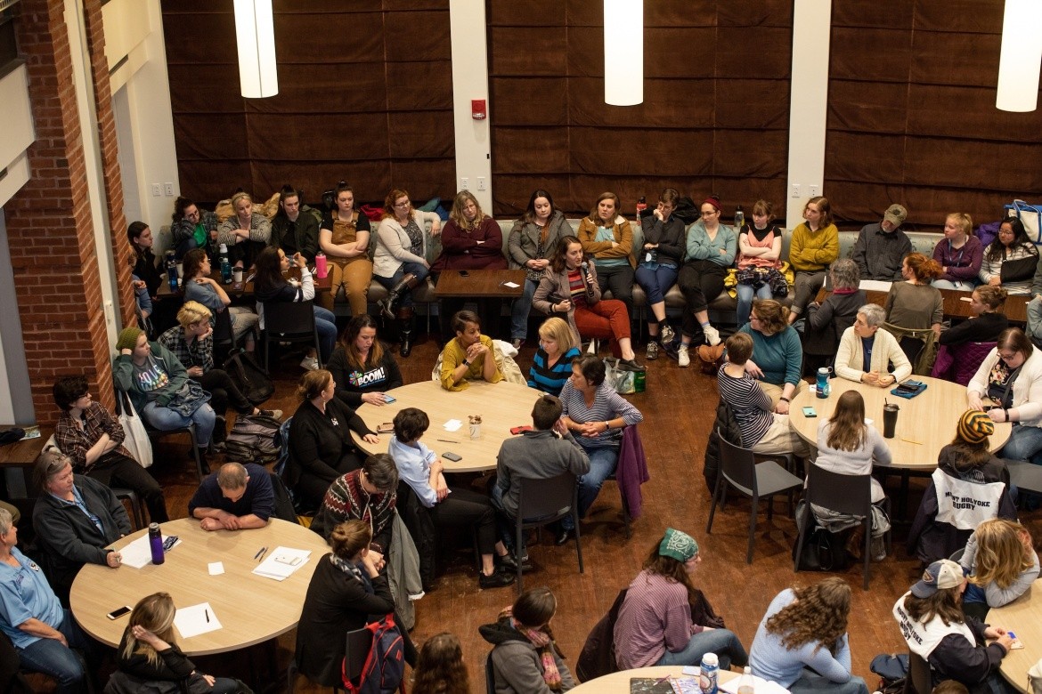 Aerial view of audience sitting at tables in conversation, BOOM panel.