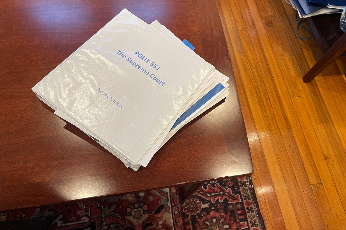 A white binder with a title page that reads "POLIT-351 The Supreme Court Danielle R. Holley" on a wooden table.