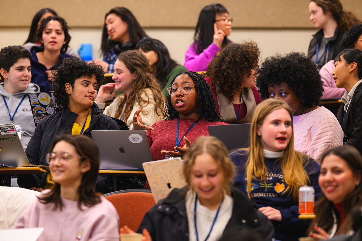 Students sit in rows of a classroom, many in discussion.