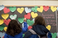 Students standing at a blackboard covered with stickynote hearts containing messages about disability
