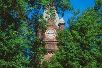 Mount Holyoke College's Clocktower slightly obscured by green leaves with a bright blue sky.