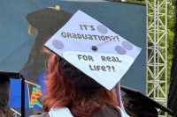 A 2024 graduate of Mount Holyoke College wearing a mortarboard decorated with the phrase “It’s graduation?! For real life?!”