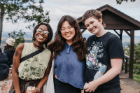 Three students smiling widely on the top of Mount Holyoke on Mountain Day 2022
