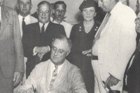 Frances Perkins looks on as President FDR signs the Social Security Act into law.