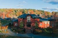 An aerial view of Mount Holyoke’s Blanchard Hall and Community Center in waning afternoon light, with colorful fall foliage and a blue sky in the background.