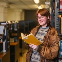 Charlie Watts, class of 2025, in the library with an open book.