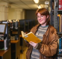 Charlie Watts, class of 2025, in the library with an open book.