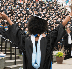 A student with arms raised after receiving their degree
