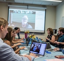 Professional and Graduate students in a classroom with a large screen for online students, showing an example of hybrid learning environment.