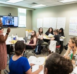 MATM students in a classroom discussion with a digital screen displaying other engaged students.