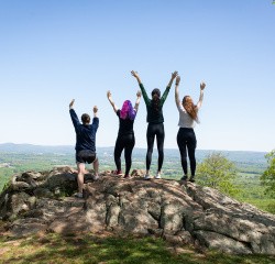 Four seniors cheering with arms raised at the top of Mount Holyoke