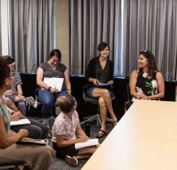 Professional and Graduate students in a group discussion where several students are smiling and holding notebooks
