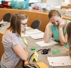 A group of three PaGE students looking at numbers on green cards on a table.