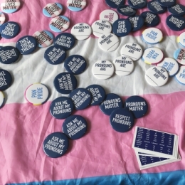 A selection of buttons with sayings such as "Ask Me About My Pronouns" and "Trans Lives Matter"