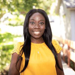 Amanda Awadey - a black woman wearing yellow and smiling - on the Mount Holyoke campus in 2023