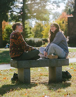 Two students are chatting on a bench on the Mount Holyoke campus.