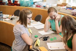A group of three PaGE students looking at numbers on green cards on a table.
