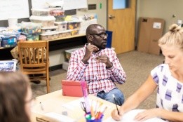 Professional and Graduate student in a classroom, explaining something and gesturing while others take notes